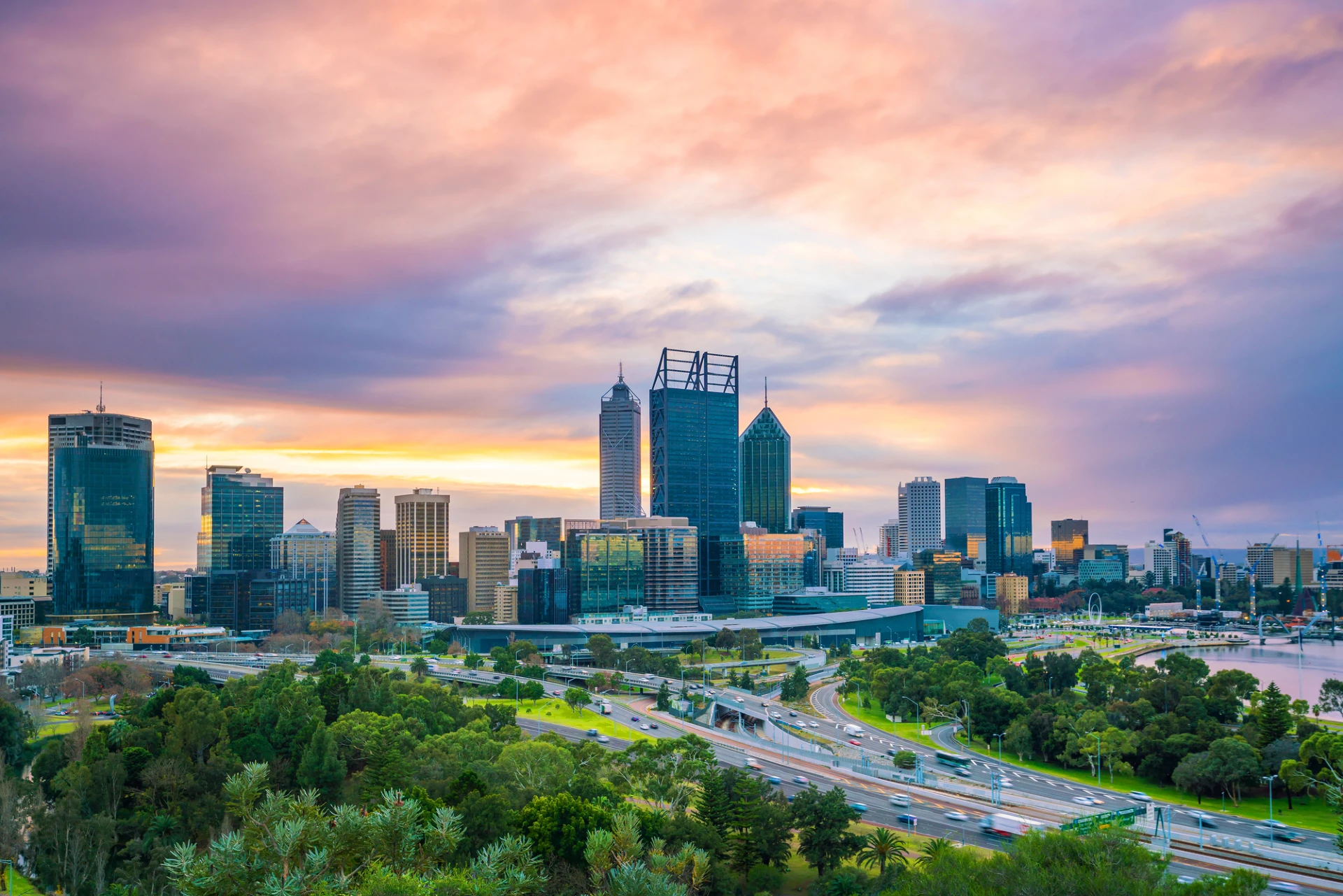 a photo of the perth skyline at sunset. high rise buildings and freeways in the foreground.
